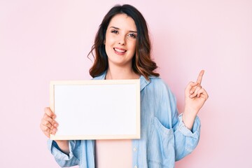 Young beautiful brunette woman holding blank empty banner smiling happy pointing with hand and finger to the side