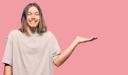 Handsome caucasian man with long hair wearing casual clothes smiling cheerful presenting and pointing with palm of hand looking at the camera.