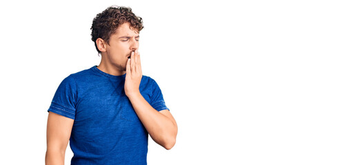 Young handsome man with curly hair wearing casual clothes bored yawning tired covering mouth with hand. restless and sleepiness.