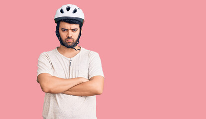 Young hispanic man wearing bike helmet skeptic and nervous, disapproving expression on face with crossed arms. negative person.