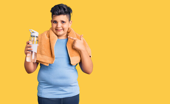 Little boy kid wearing sportswear drinking bottle of water smiling happy pointing with hand and finger