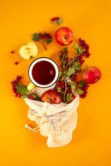 Red garden organic apples, hawthorn berries in a mesh bag and cup of hot spiced tea on an orange background. Autumn still life flat lay