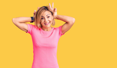 Young blonde woman wearing sportswear posing funny and crazy with fingers on head as bunny ears, smiling cheerful