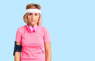 Young blonde woman wearing sportswear and headphones with serious expression on face. simple and natural looking at the camera.