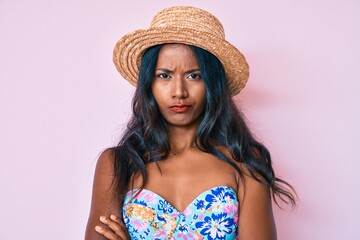 Young indian girl wearing bikini and summer hat skeptic and nervous, disapproving expression on face with crossed arms. negative person.