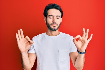 Young hispanic man wearing casual white tshirt relaxed and smiling with eyes closed doing meditation gesture with fingers. yoga concept.