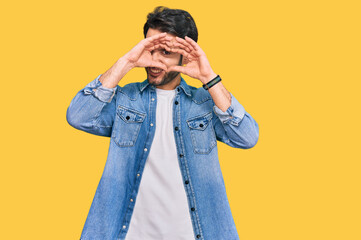 Young hispanic man wearing casual clothes doing heart shape with hand and fingers smiling looking through sign