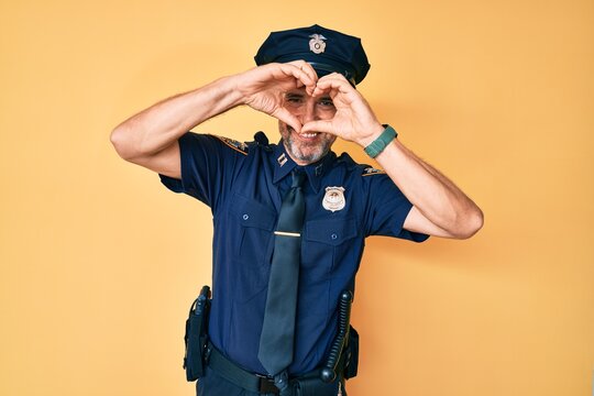 Middle age hispanic man wearing police uniform doing heart shape with hand and fingers smiling looking through sign
