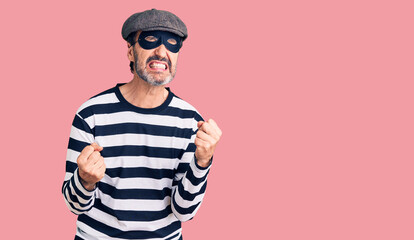 Middle age handsome man wearing burglar mask very happy and excited doing winner gesture with arms raised, smiling and screaming for success. celebration concept.