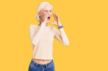 Young blonde woman wearing casual clothes shouting angry out loud with hands over mouth