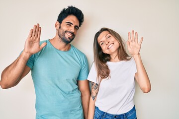Beautiful young couple of boyfriend and girlfriend together waiving saying hello happy and smiling, friendly welcome gesture