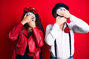 Couple wearing day of the dead costume over red covering eyes and mouth with hands, surprised and shocked. hiding emotion