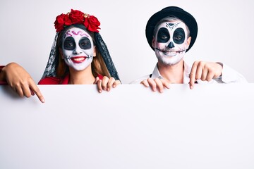 Couple wearing day of the dead costume holding blank empty banner smiling happy pointing with hand and finger