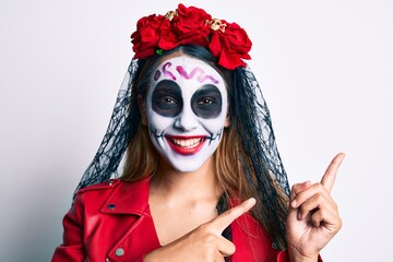 Woman wearing day of the dead costume over white smiling and looking at the camera pointing with two hands and fingers to the side.