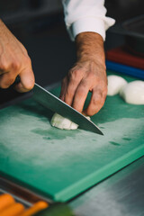 professional chef slicing onions over a green board in the restaurant kitchen