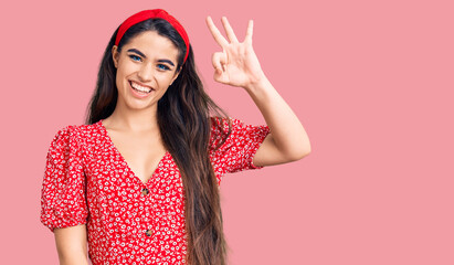 Brunette teenager girl wearing summer dress smiling positive doing ok sign with hand and fingers. successful expression.