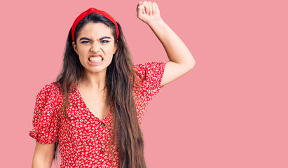 Brunette teenager girl wearing summer dress angry and mad raising fist frustrated and furious while shouting with anger. rage and aggressive concept.