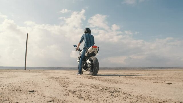 Man biker doing tire burnout in the desert, slow motion. Professional motorcyclist drifting on street bike on a dry salt lake and ride away