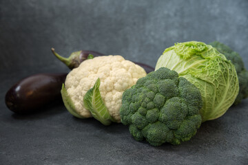 Three types of cabbage, Brassica oleracea sabauda, broccoli, cauliflower and eggplant on a gray background
