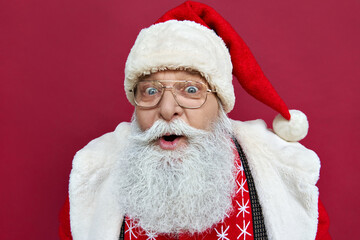 Surprised excited funny old bearded Santa Claus face wearing glasses costume looking at camera,...