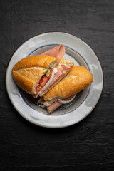 Mexican ham sandwich with avocado and cheese also called torta on dark background