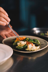 Close-up of the hands of a male chef decorating with carrot in ceramic dish over stainless steel worktop in restaurant kitchen.