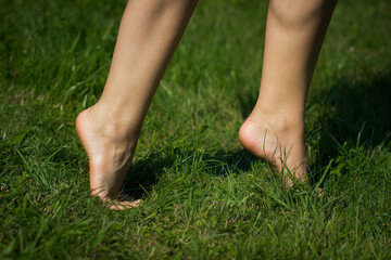 Close up side view of female legs standing tiptoe on green grass. Barefoot young woman. Tiptoeing.