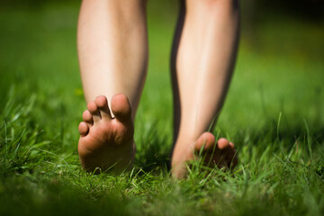 Woman's barefoot walking on the fresh, green grass in the sunny morning. Healthy lifestyle.