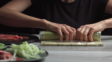 Japanese chef prepares sushi rolls with salmon and avocado. Cook hands making Japanese sushi roll on the bamboo mat. Delicious Japanese food, low-angle view