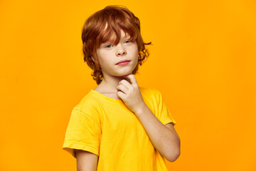 A boy with red hair holds his hand near his face and looks ahead