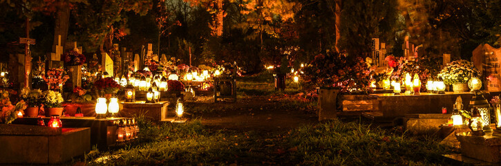 Many lit grave lights on All Saints' Day. Grave memorial candles in the cemetery. Cemetery alley at night.  - obrazy, fototapety, plakaty