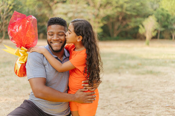 Latin family celebrating Easter. Curly girl wearing bunny ears and kissing her father on a sunny day in the park