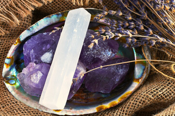 An image of an abalone shell filled with amethyst crystals and white selenite on old burlap...