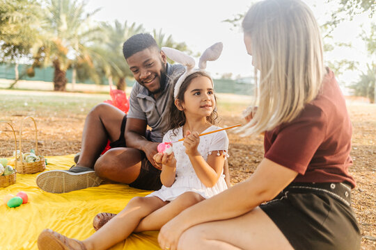 Latin family celebrating Easter. curly girl wearing bunny ears and painting an easter egg