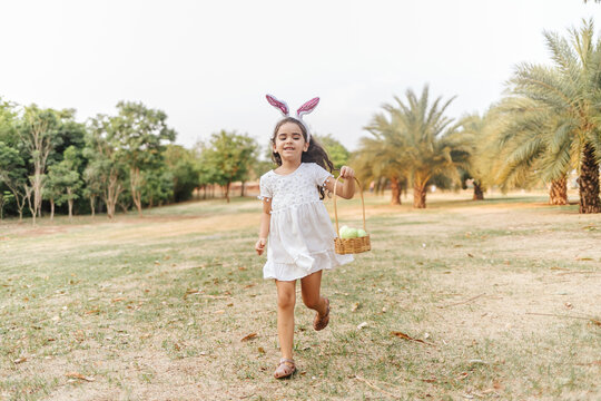 Curly girl with bunny ears running and holding a hamper of easter eggs in the park