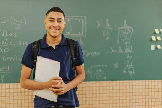 Latin men student smiling wearing backpack holding a notebook in a classroom