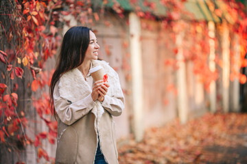 Fall concept - beautiful woman drinking coffee in autumn park under fall foliage