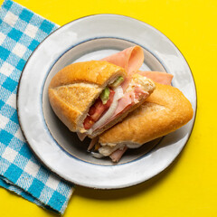Mexican ham sandwich with avocado and cheese also called torta on yellow background