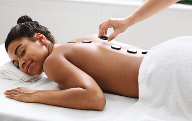 Obraz na płótnie Canvas Joyful black lady having hot stone massage at luxury spa