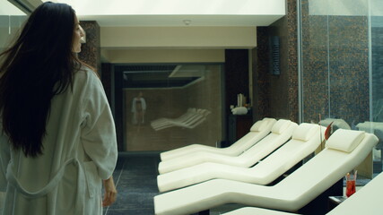 Sexy woman taking off bathrobe in spa center. Pretty girl relaxing on deckchair.