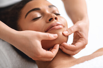 Massage therapist rubbing relaxed black lady chin