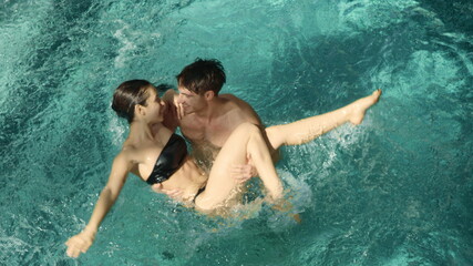 Romantic pair hugging in pool indoors. Man holding woman in arms in thermal pool