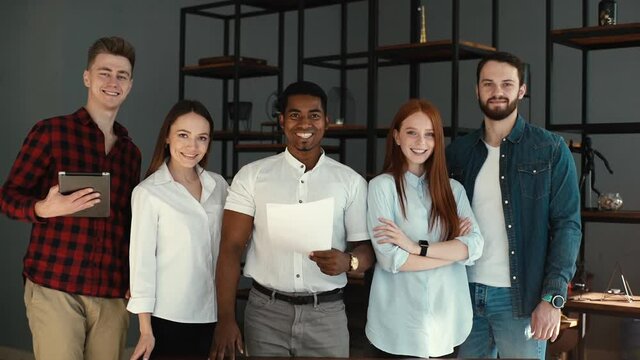 Portrait of successful smiling multi-ethnic business team in modern office. Cheerful multiracial professionals young business people or company staff standing together, posing in conference room.