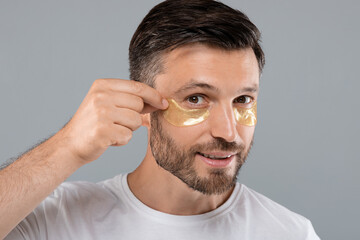 Excited attractive man applying eye patches on his face