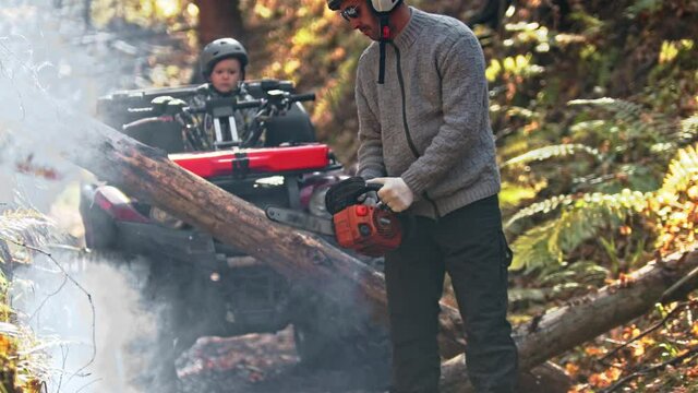 An autumn forest - man turns on a chainsaw in the forest and his son is waiting for him on a quad bike