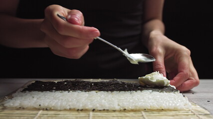 Close up of female hands of professional chef in gloves making delicious sushi rolls in restaurant kitchen