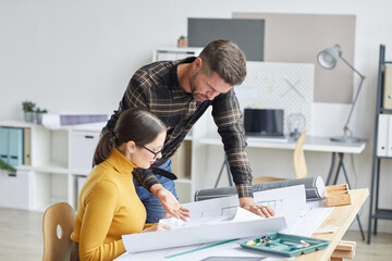 Side view portrait of two architects collaborating on blueprints while working in office together,...