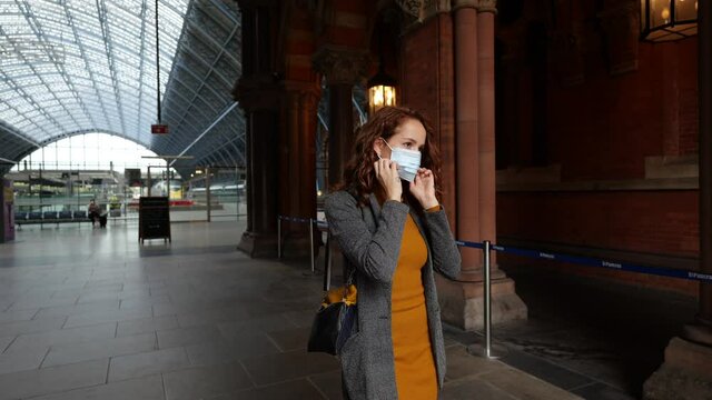 Red haired woman outside train station putting on a facemask