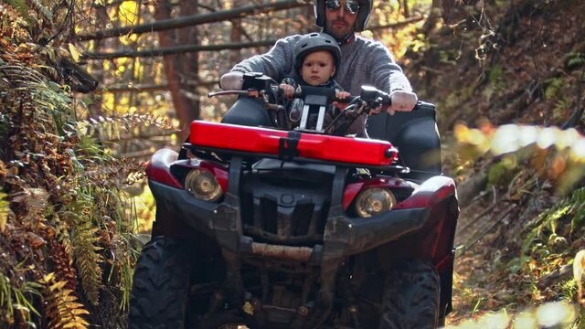 Outdoor autumn activities - father with son riding a quad bike in the woods