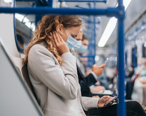 passengers in protective masks using their gadgets in the subway car .